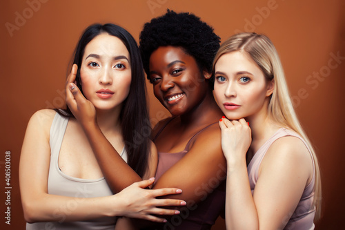 young pretty asian, caucasian, afro woman posing cheerful together on brown background, lifestyle diverse nationality people concept