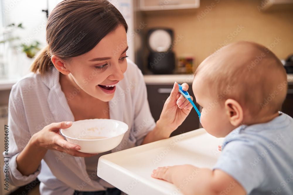 Positive delighted young parent feeding her baby Positive delighted young parent feeding her baby