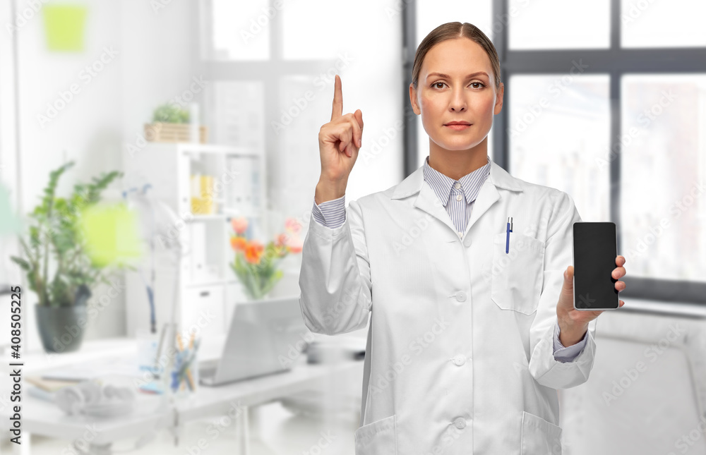 medicine, profession and healthcare concept - female doctor in white coat with smartphone pointing finger up over medical office at hospital on background medicine, profession and healthcare concept - female doctor in white coat with smartphone pointing finger up over medical office at hospital on background