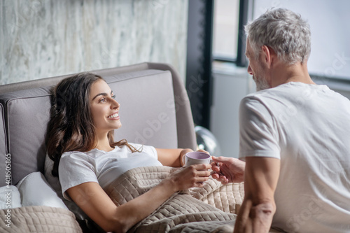 Man giving coffee to woman lying in bed