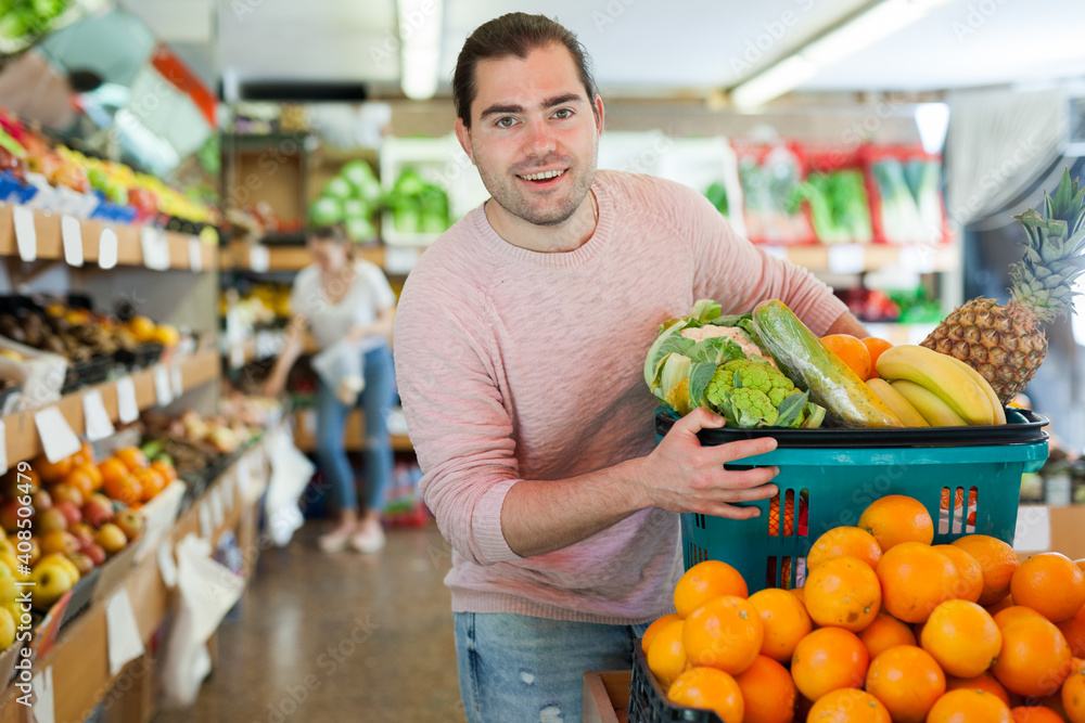 Smiling man standing with full grocery cart during shopping in fruit shop