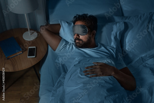 people, bedtime and rest concept - indian man in eye mask sleeping in bed at home at night photo