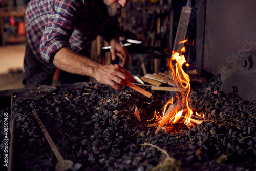 Male Blacksmith Lighting Wood Kindling To Start Blaze In Forge
