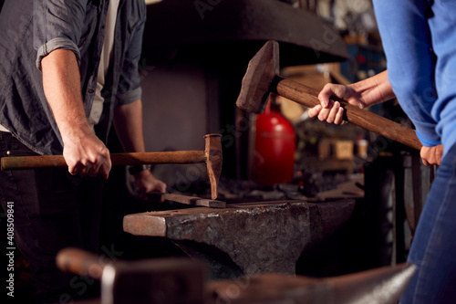 Close Up Of Two Blacksmiths Hammering Metalwork On Anvil