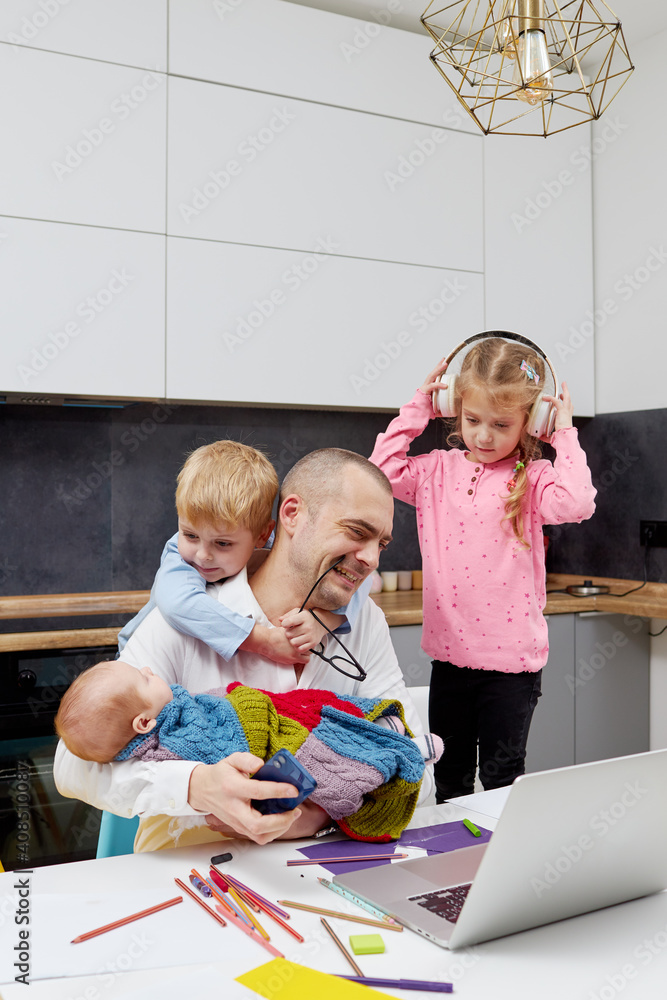 Fototapeta premium Father with a newborn baby in arms working from home during quarantine and closed school. coronavirus outbreak. Young businessman freelancer works on laptop with children playing around.