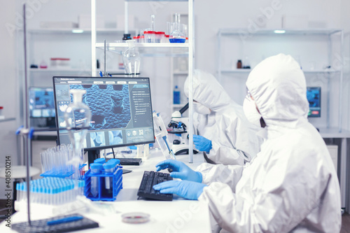 Chemist in ppe suit typing on keyboard checking virus development in equipped laboratory. Medical engineer using computer during global pandemic with coronavirus dressed in coverall.