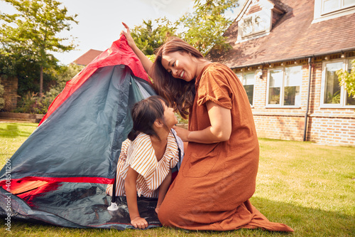 Asian Mother With Daughter In Garden At Home Putting Up Tent For Camping Trip Together