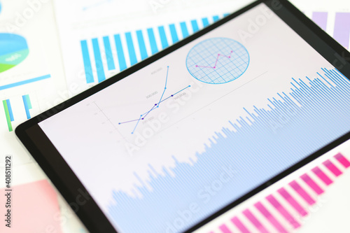 Digital tablet with graphs and charts lying on documents closeup