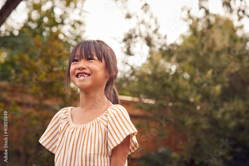 Portrait Of Smiling Asian Girl With Missing Front Teeth Having Fun In Garden At Home