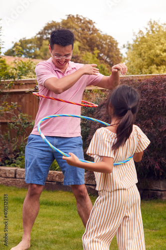 Asian Father And Daughter Having Fun Playing With Hula Hoop In Garden At Home