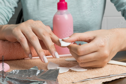 Removing gel Polish from nails. Woman pours remove liquid on a cotton pad, puts it on a nail and wraps the foil. Removing shellac nails. Do a manicure for yourself at home. Beauty, skin care, routine. photo