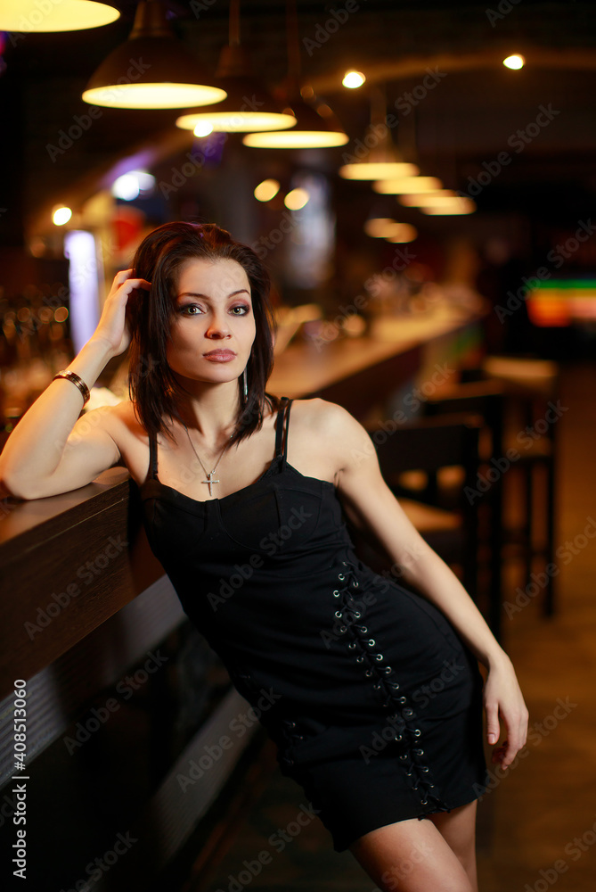 Beautiful brunette woman in evening dress posing near bar alone