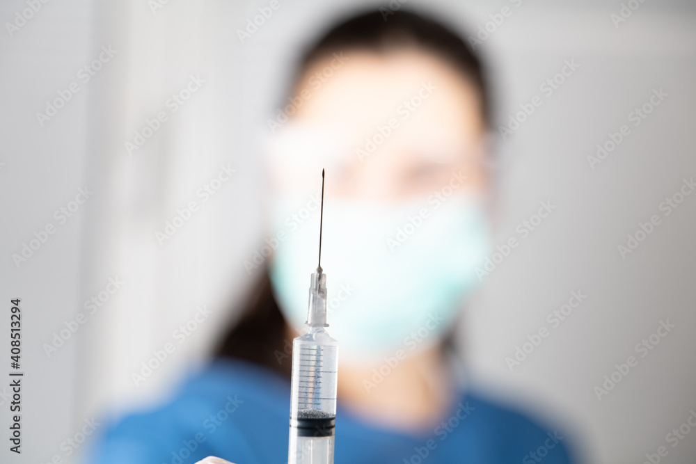 blurred doctor holding focused on filling with medication syringe with needle, with a drop of serum or drug. Vaccination, Coronavirus, immunization concept. Blurred background blurred doctor holding focused on filling with medication syringe with needle, with a drop of serum or drug. Vaccination, Coronavirus, immunization concept. Blurred background