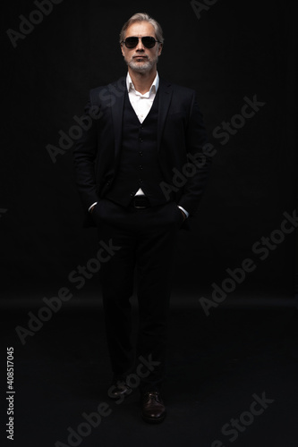 Portrait of a respectable mature man in a suit and sunglasses on a black background. Businessman portrait. Copy space.