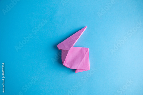 Step-by-step instructions for creating  origami bunny out of colored paper on  blue background, for  decorative Easter party decoration or for small Easter gifts.