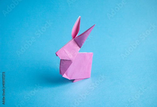 Step-by-step instructions for creating  origami bunny out of colored paper on  blue background, for  decorative Easter party decoration or for small Easter gifts.