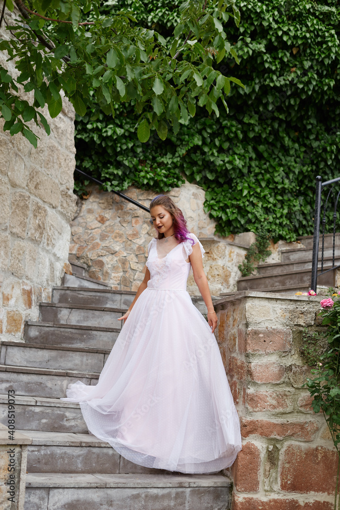 Obraz premium Beautiful woman with purple hair in a white wedding dress walks in the garden. Natural makeup
