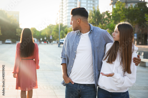 Disloyal man looking at another woman while walking with his girlfriend outdoors photo