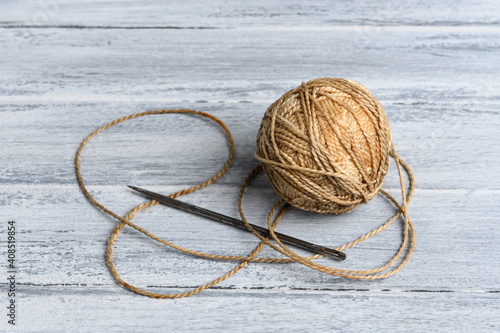 An old, rusty, long needle and a ball of strong, thick thread on a gray-painted table