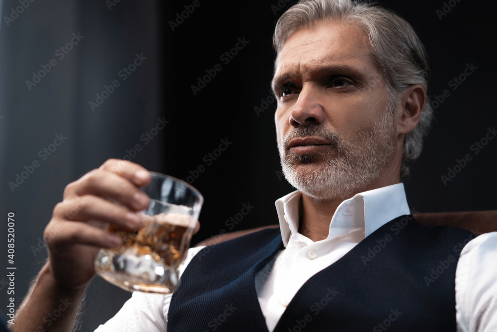 Portrait of handsome elegant mature man with a glass whiskey in a dark room.