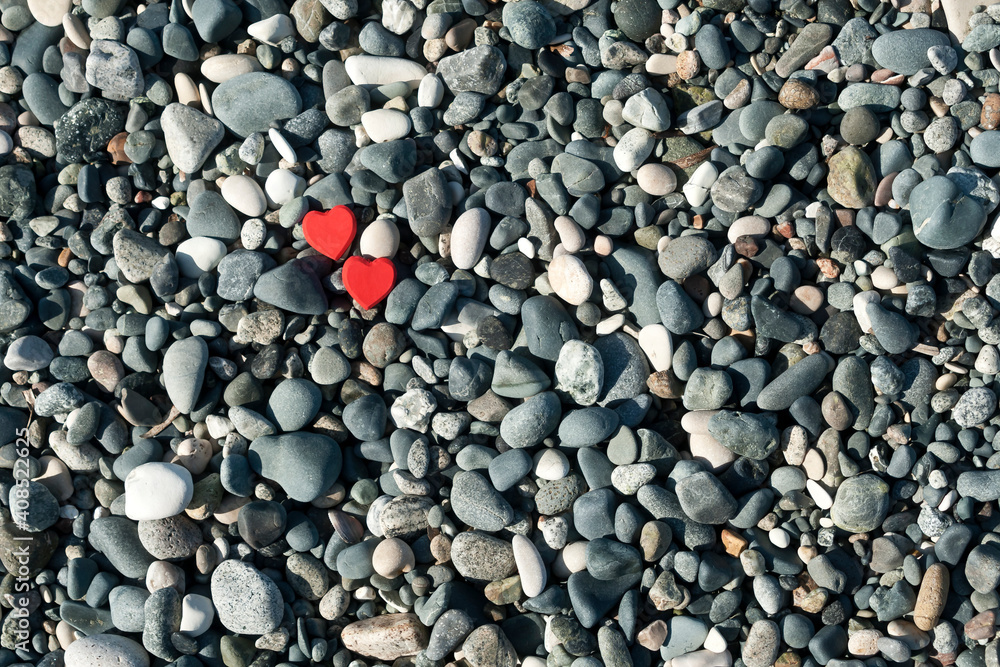Two red hearts among beach stones background Two red hearts among beach stones background