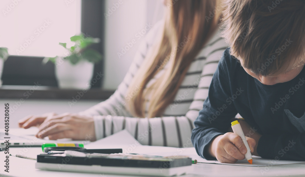 The kid is drawing while his mom working with laptop The kid is drawing while his mom working with laptop