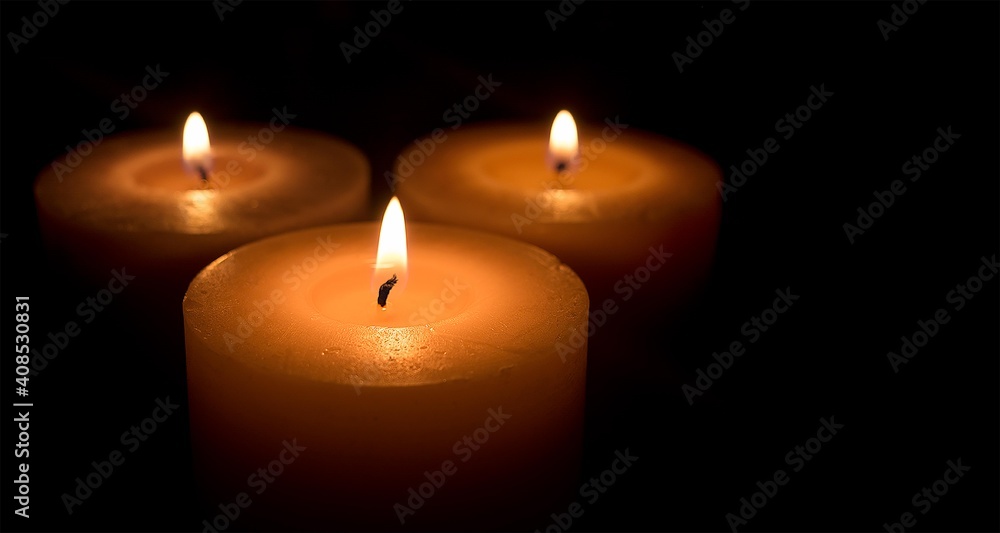 Three large white candles burn in the dark close-up. Banner with space for text. Three large white candles burn in the dark close-up. Banner with space for text.