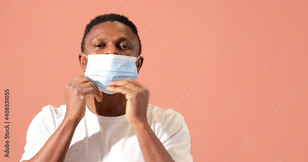 African-American man putting on medical mask against color background African-American man putting on medical mask against color background
