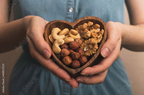 Woman holding heart shaped plate with mixed nuts. Healthy organic food. Close up