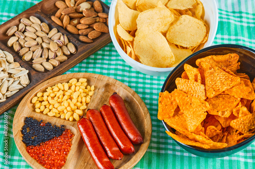 Assorted snacks, bowl of chips and a plate of sausages on a blue table