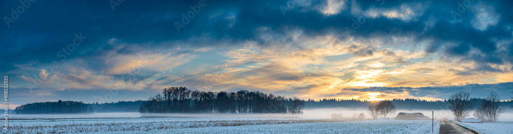 Landscape panorama with road, white fields cover by snow and sunset sky.