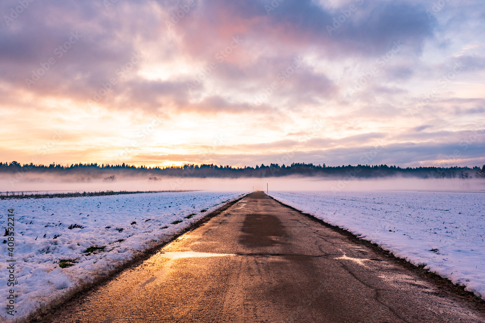 Winter landscape with road, white fields cover by snow and sunset sky.