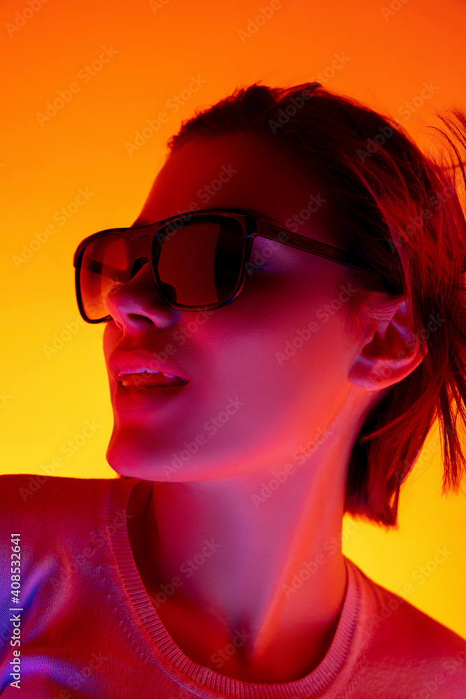 Confidence. Caucasian woman's portrait on orange studio background in red-pink neon light. Beautiful female model in sunglasses. Concept of human emotions, facial expression, sales, ad, fashion. Confidence. Caucasian woman's portrait on orange studio background in red-pink neon light. Beautiful female model in sunglasses. Concept of human emotions, facial expression, sales, ad, fashion.