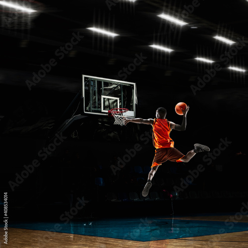 Champion. African-american young basketball player in action and motion in flashlights over dark gym background. Concept of sport, movement, energy and dynamic, healthy lifestyle. Arena's drawned. © master1305