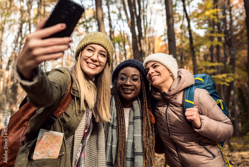 Fotografia, Obraz Three female friends enjoying hiking in forest and making selfie with smartphone