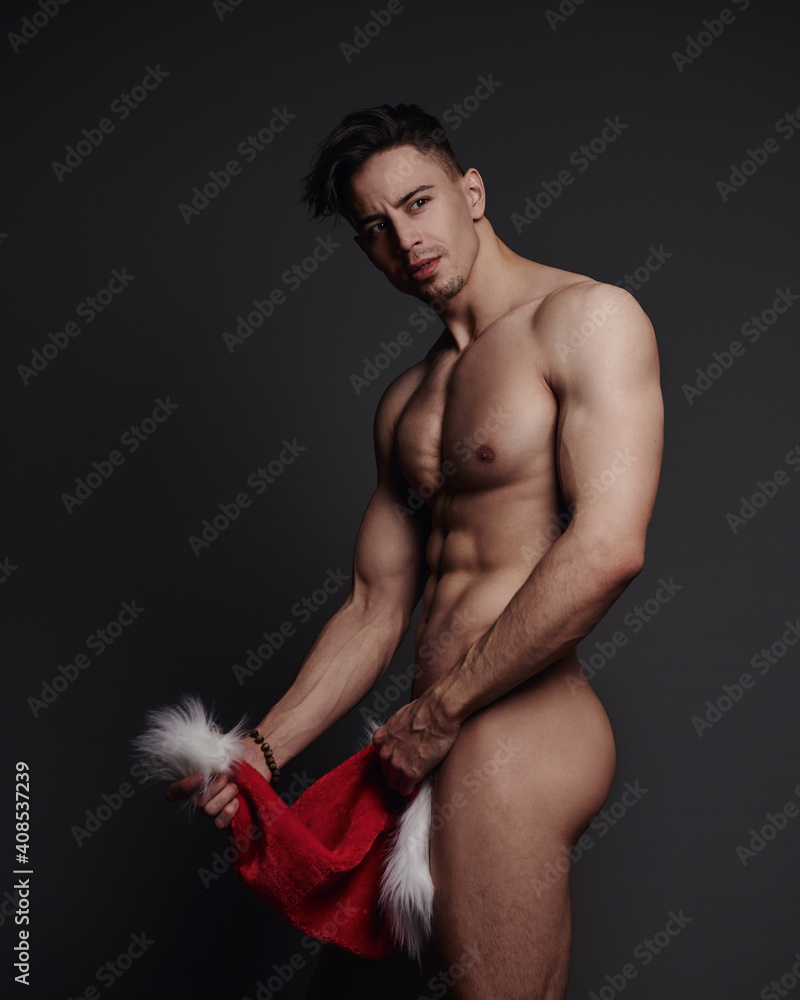 Naklejka premium Naked handsome man covering himself with Santa hat 