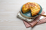 Homemade Spanish tortilla with one slice cut - omelette with potatoes on plate on white wooden rustic background top view. Traditional dish of Spain Tortilla de patatas for lunch or snack, overhead
