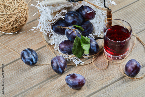 Garden plums in a basket on a wooden table with a glass of juice