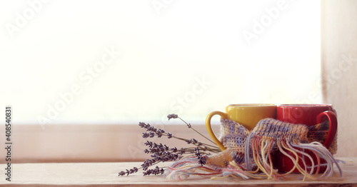 red and yellow cups are wrapped in a purple scarf and decorated with a lavender bouquet against the background of the window. date with the aroma of coffee