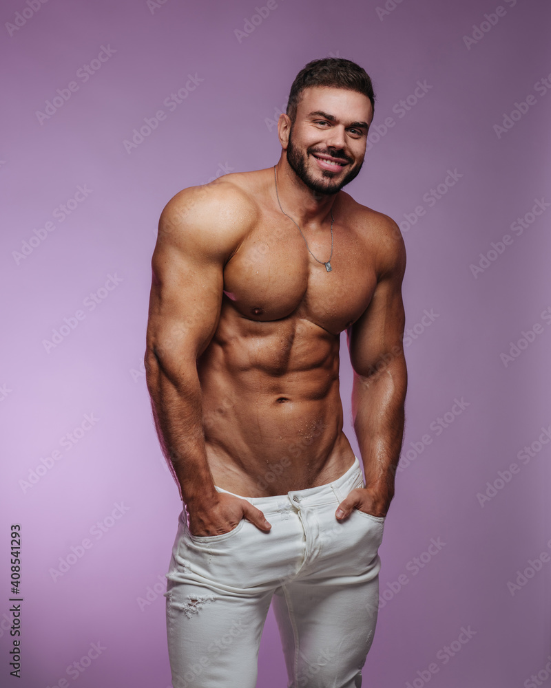 Fototapeta premium Male fitness model in white jeans standing at pink background