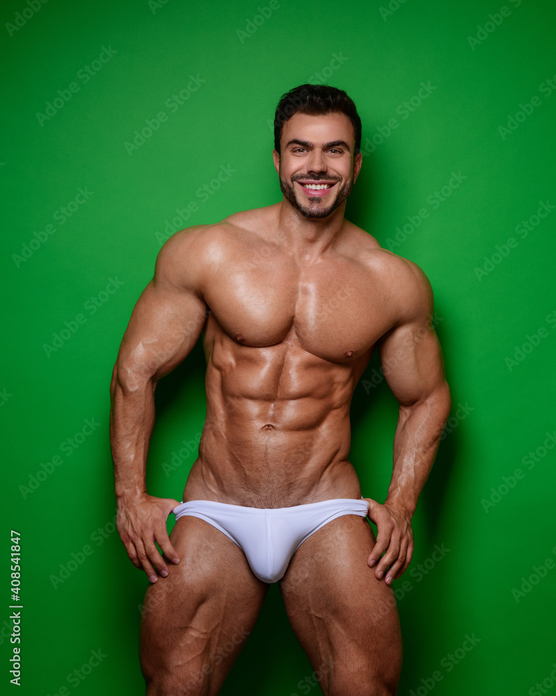Fototapeta premium Smiling male model in white swimwear at green background