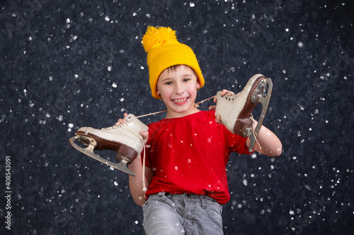 Handsome little boy in a knitted yellow hat with vintage skates on a gray background.