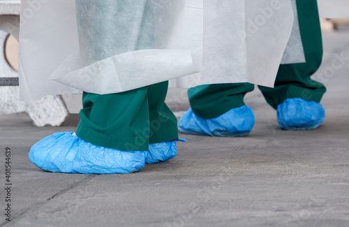Tablou pe pânză Close up feet of health workers in PPE clothing and blue protective plastic bags