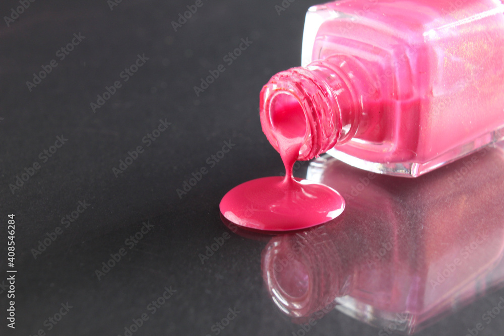 Pink nail polish is poured out of the bottle bottle on a black background with a copyspace place for text Pink nail polish is poured out of the bottle bottle on a black background with a copyspace place for text