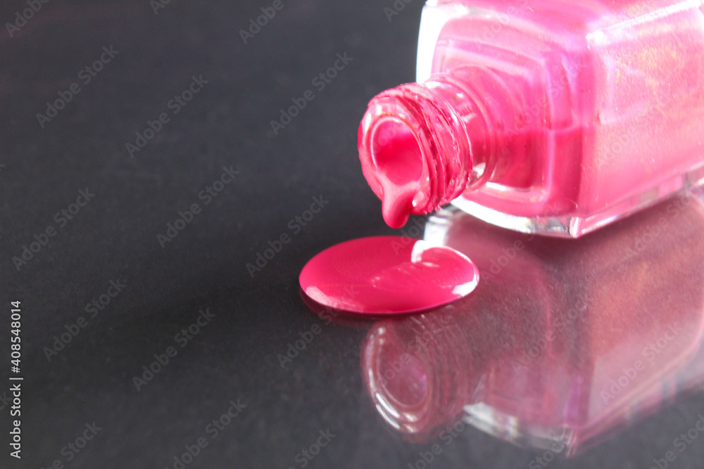 Pink nail polish is poured out of the bottle bottle on a black background with a copyspace place for text Pink nail polish is poured out of the bottle bottle on a black background with a copyspace place for text