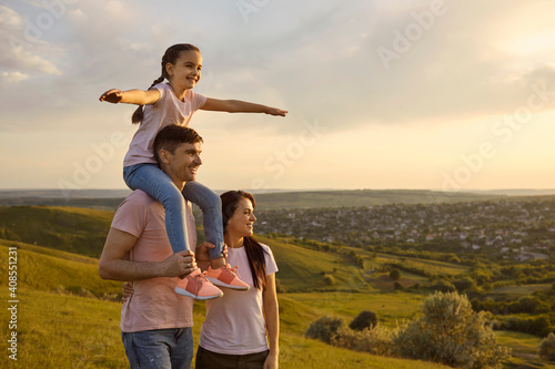 Happy parents with a child on their shoulders play in nature. photo