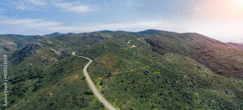 Empty long mountain road to the horizon on a sunny summer day at bright sunset - aerial drone shot