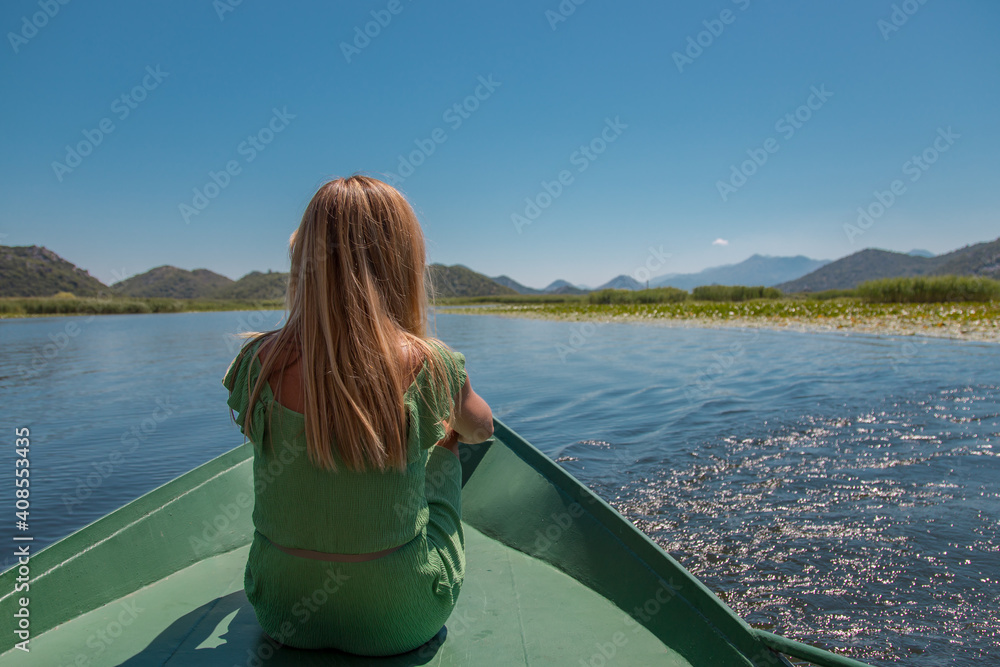 Happy carefree woman in travels by boat.
Traveller woman enjoying open spaces on lake, serenity in nature.  The concept of outdoor activities and tourism in nature. Skadar lake in Montenegro.