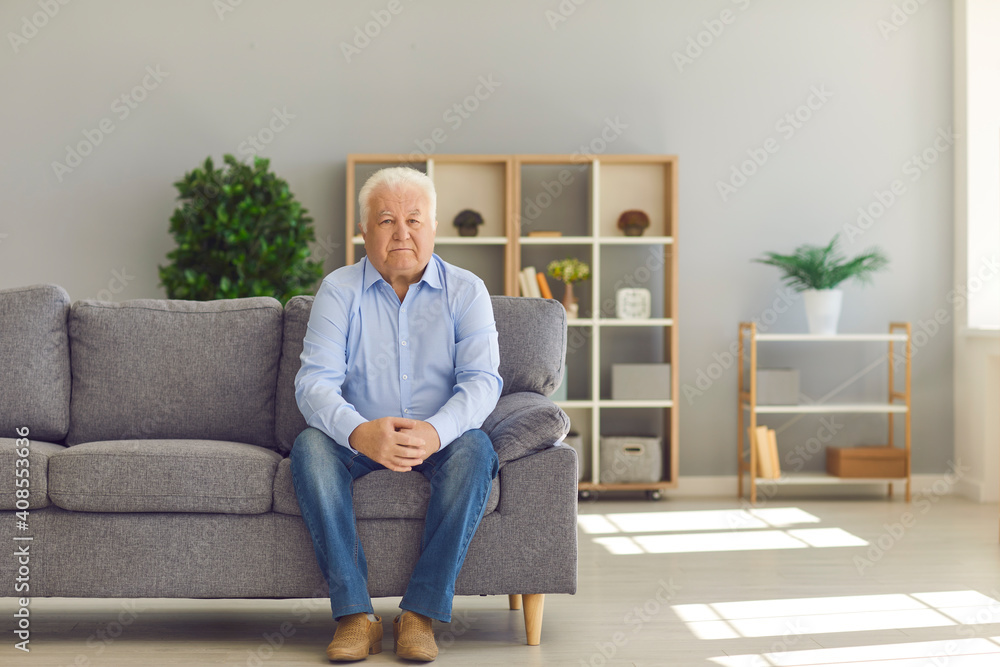 White-haired senior man sitting alone on couch at home and thinking about his life