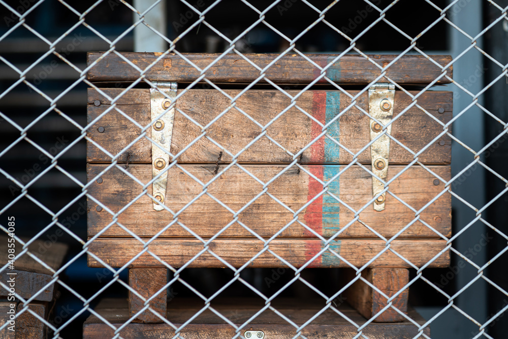 An antique wooden box cage is keep in storage, barricaded by wire mesh fence (Blurred as foreground). Like it contain some dangerous item inside. An antique wooden box cage is keep in storage, barricaded by wire mesh fence (Blurred as foreground). Like it contain some dangerous item inside.